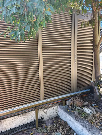 Portón corredera de aluminio con lamas tipo celosía y puerta peatonal integrada, sobre riel para motor